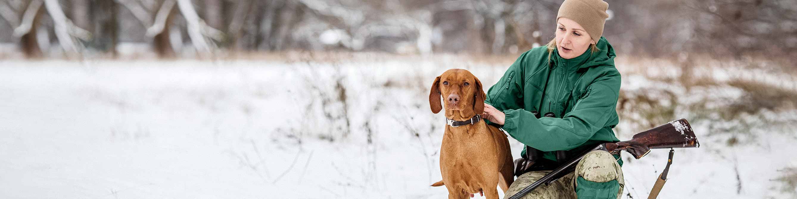 Jägerin mit Hund auf schneebedeckter Wiese