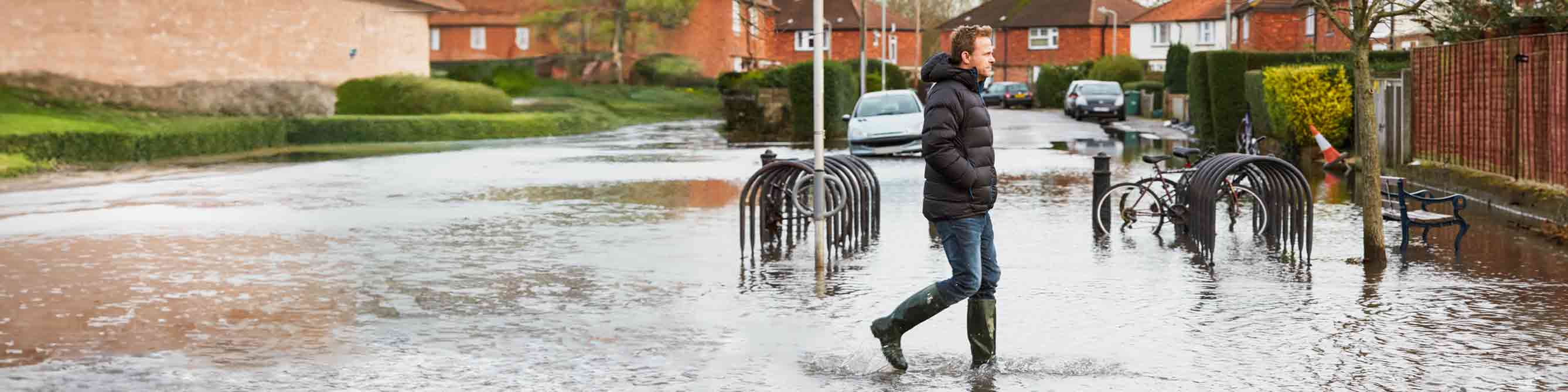 Ein Mann in Gummistiefeln läuft durch Hochwasser in einem Wohngebiet